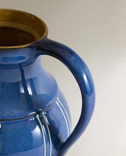 Closeup of the handles of a blue ceramic vase with white stripes