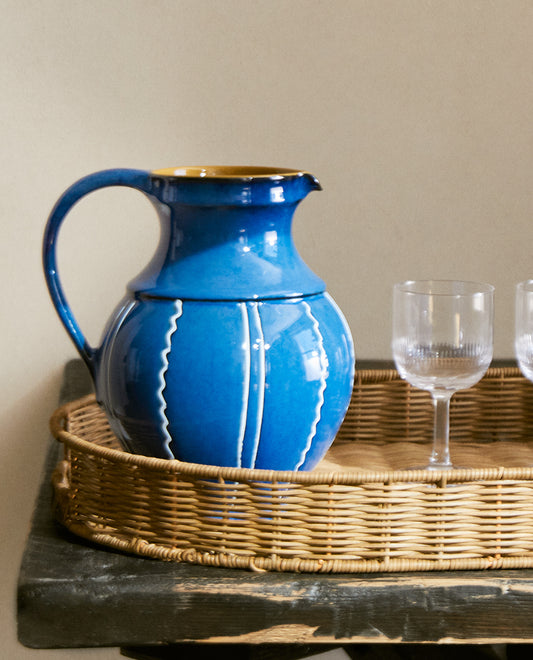 Blue ceramic vase with white stripes next to crystal glasses on a rattan tray