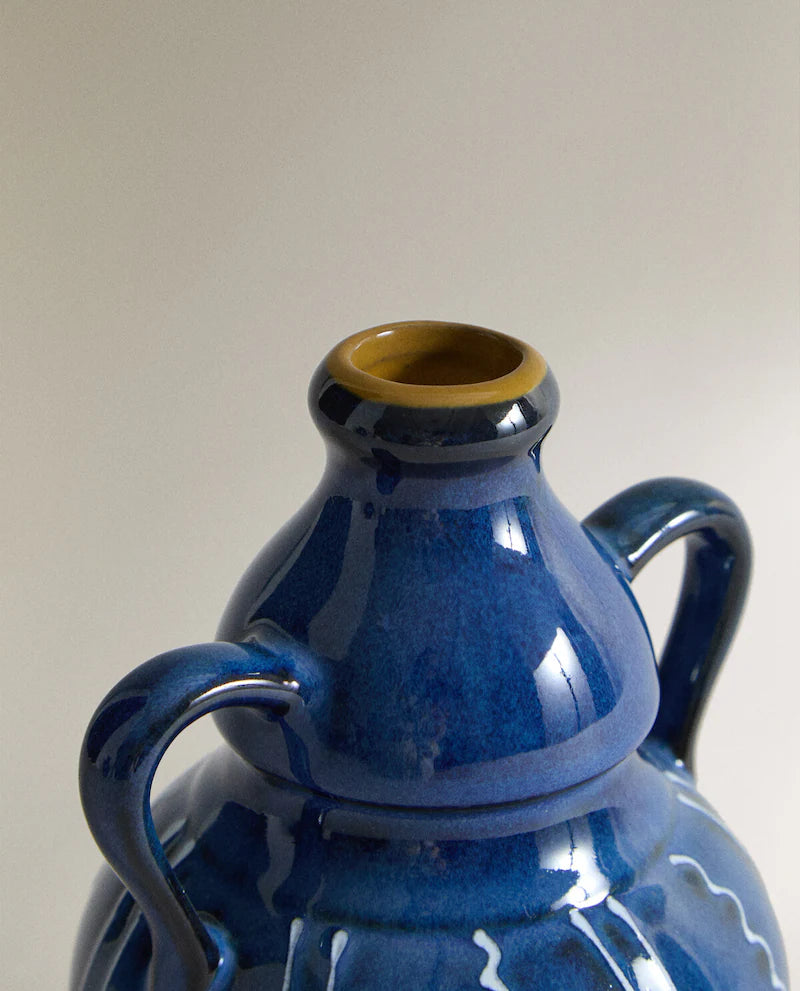 Close up of the top of a blue ceramic vase with white stripes