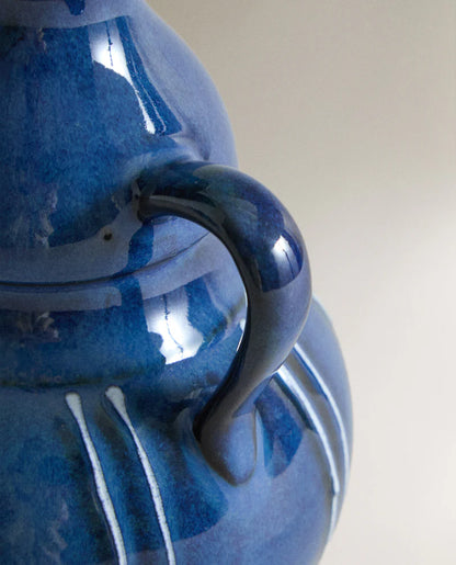 Closeup of the handles of a blue ceramic vase with white stripes